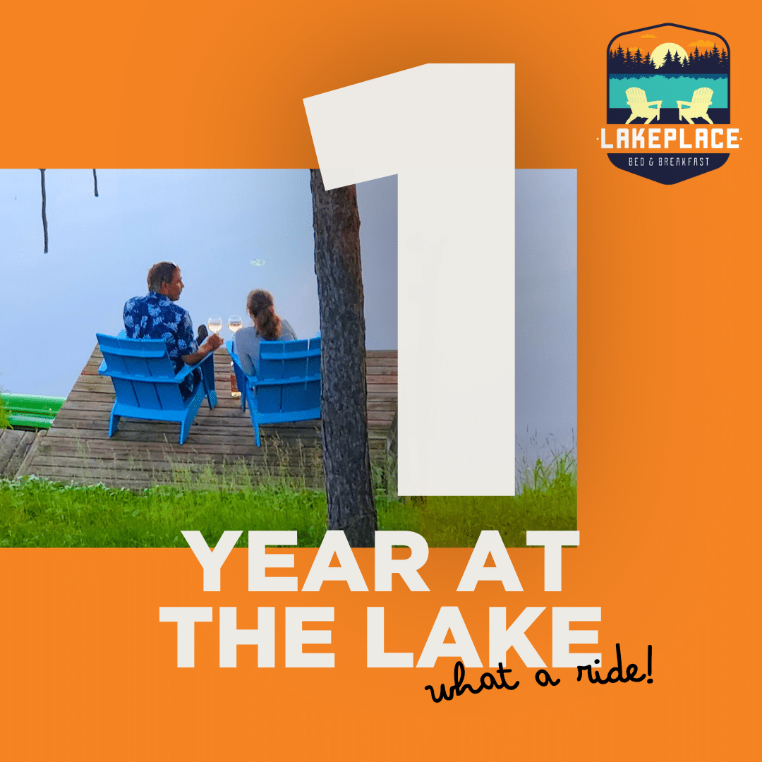 Two people enjoying a glass of wine on blue Adironack chairs next to a lake.